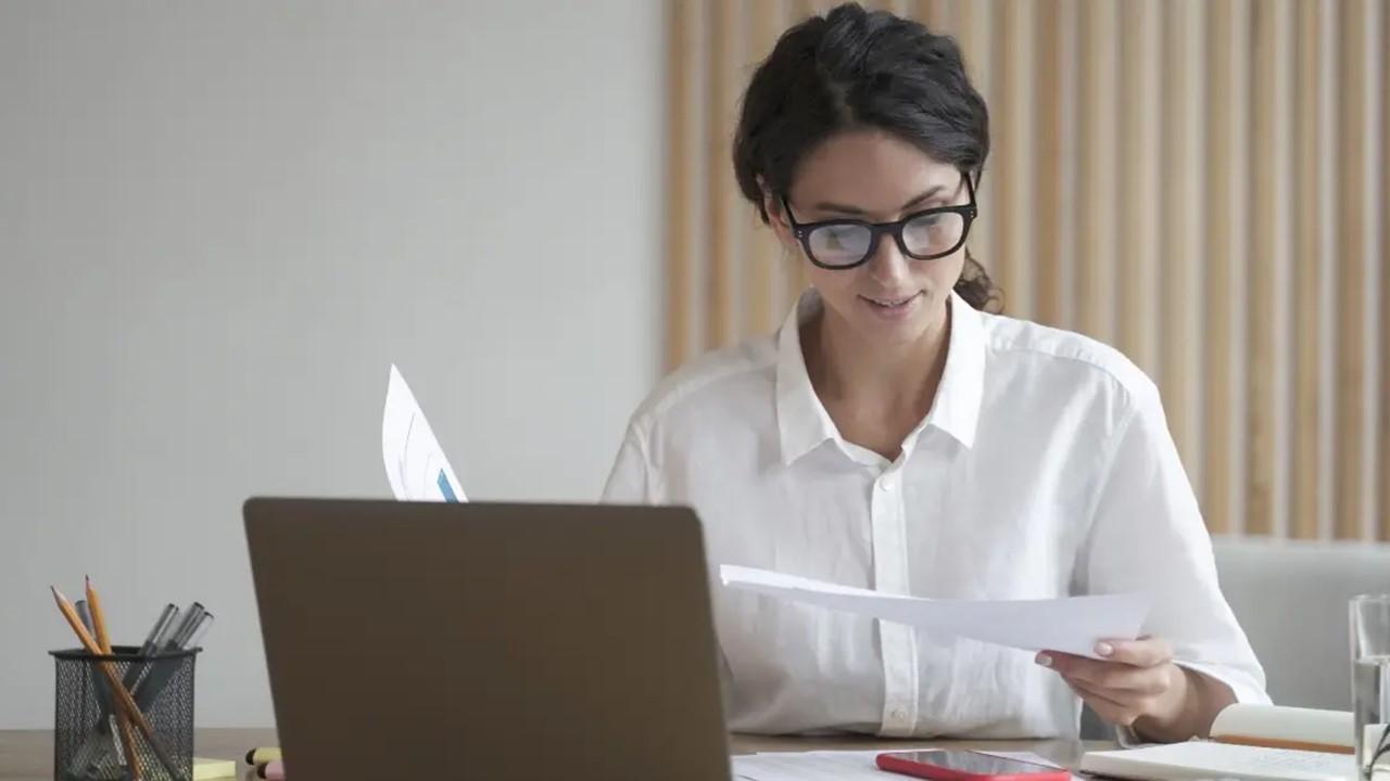 A smiling woman in a white shirt gathers her tax forms.