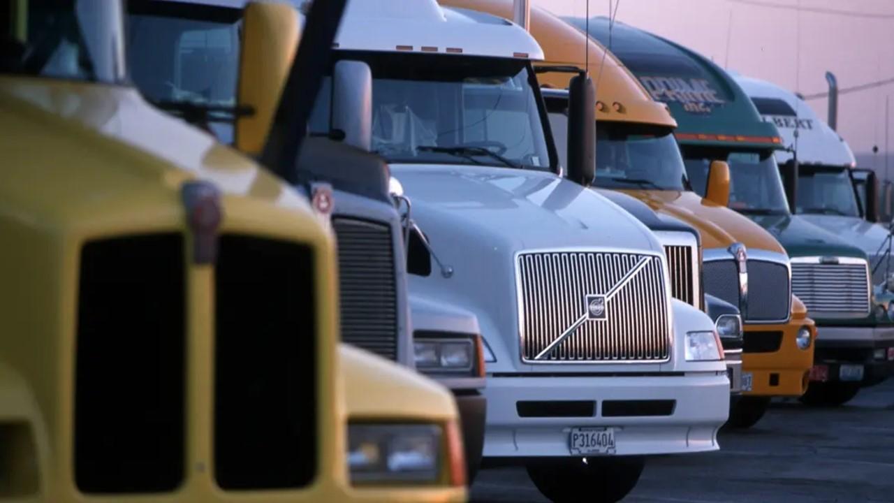 A row of semi trucks are lined up side by side in a parking lot.