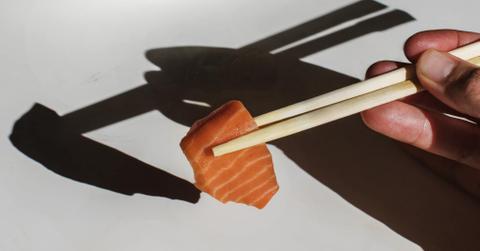 A person holding cultured salmon with chopsticks