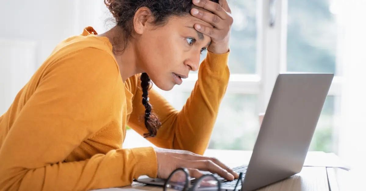 A worried woman in a yellow shirt looks at her tax forms online.