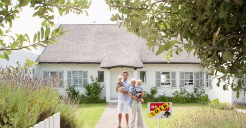 Man and woman holding babies in front of house with sold sign