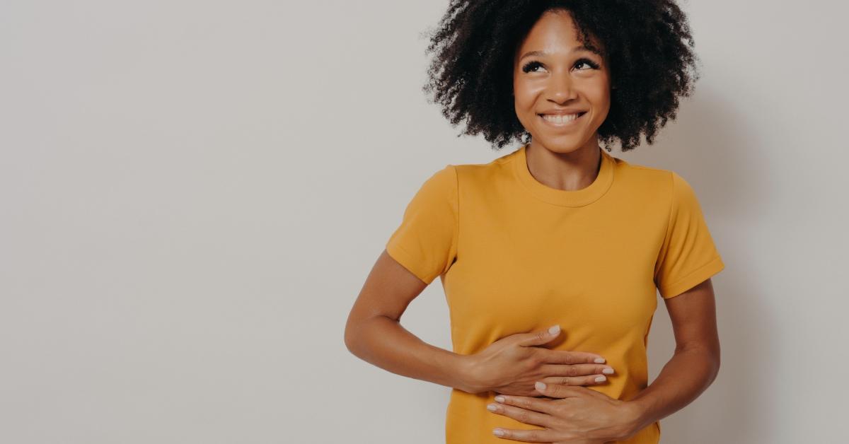 A happy woman in a yellow shirt with her hands on her stomach.