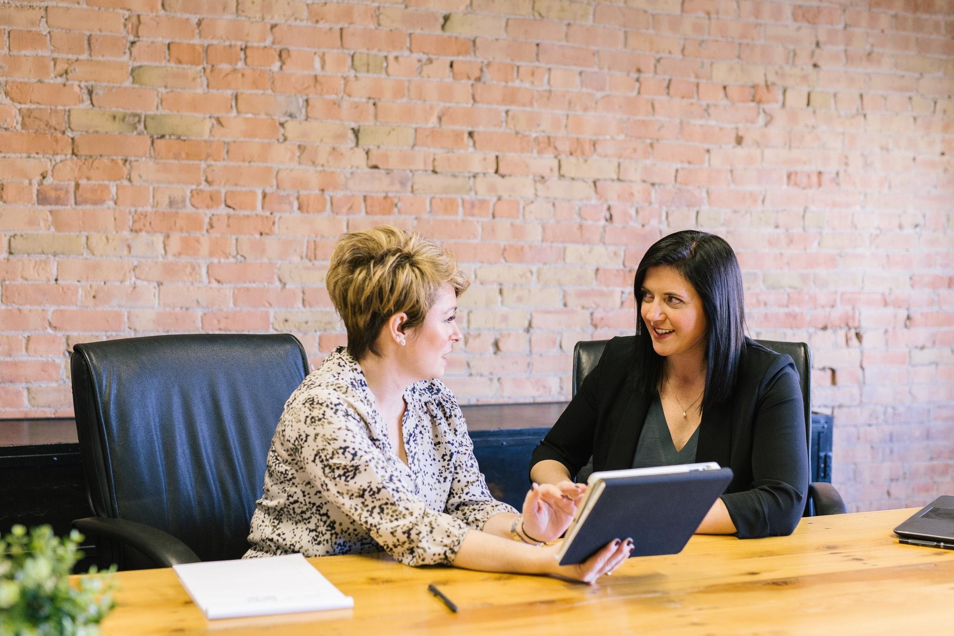 Two people sitting at a desk discussing data on a tablet 