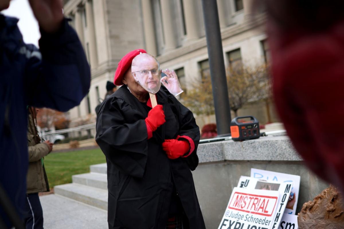 A protestor with a photo of Judge Schroeder stands outside the courtroom. 